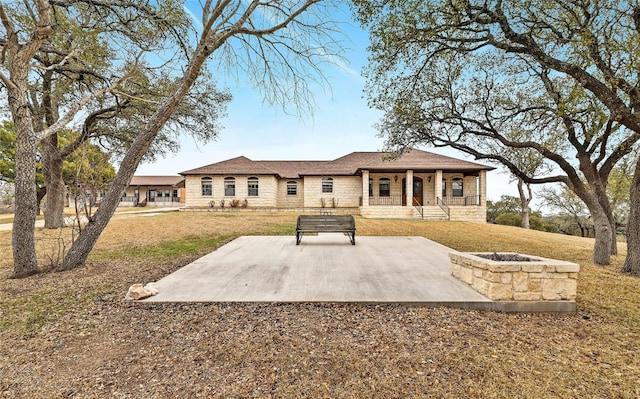 back of house with a porch, an outdoor fire pit, stone siding, and a yard