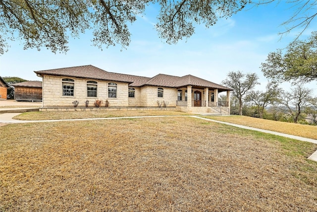 view of front of property with covered porch, stone siding, a shingled roof, and a front yard