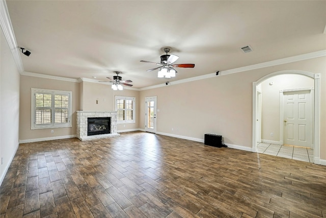 unfurnished living room with visible vents, arched walkways, wood finished floors, and ornamental molding