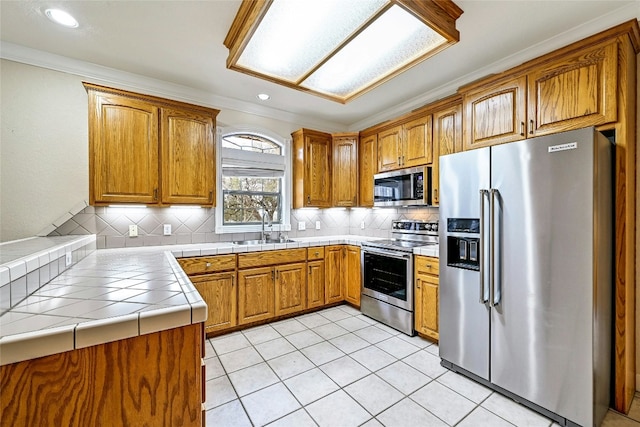 kitchen featuring brown cabinets, tile countertops, decorative backsplash, appliances with stainless steel finishes, and a sink