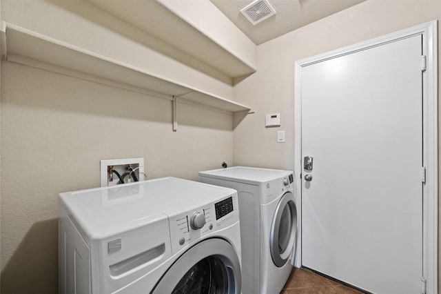 washroom with laundry area, washing machine and dryer, visible vents, and dark tile patterned flooring