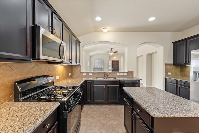 kitchen featuring arched walkways, light stone counters, a sink, vaulted ceiling, and black appliances