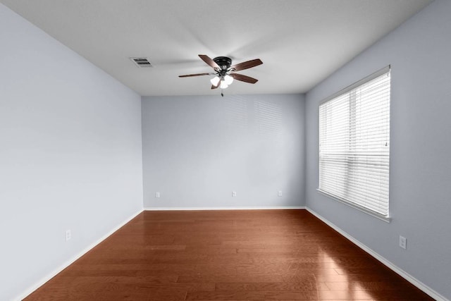 empty room featuring a ceiling fan, visible vents, baseboards, and wood finished floors