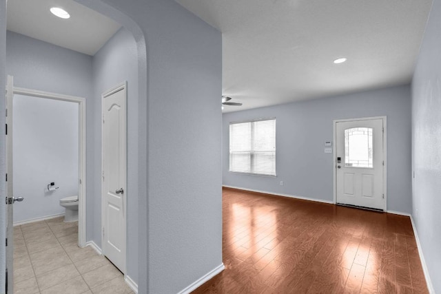 entrance foyer featuring arched walkways, light wood-type flooring, a ceiling fan, and baseboards