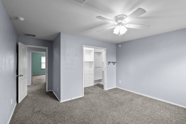 unfurnished bedroom with a textured ceiling, dark colored carpet, visible vents, and baseboards