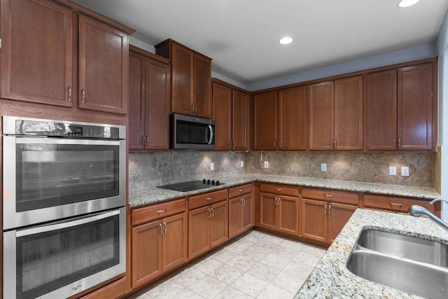 kitchen featuring stainless steel appliances, tasteful backsplash, a sink, and light stone countertops