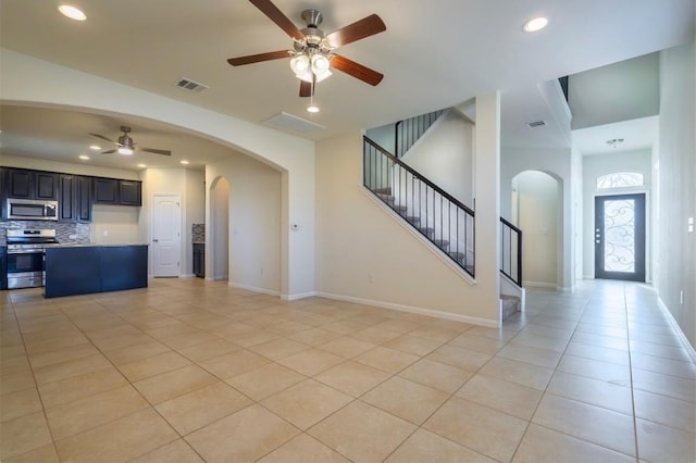 unfurnished living room with light tile patterned floors, baseboards, visible vents, arched walkways, and stairway