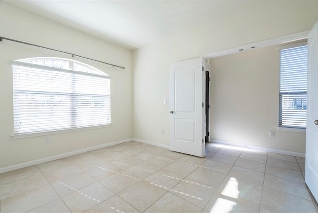 spare room featuring light tile patterned flooring, a wealth of natural light, and baseboards