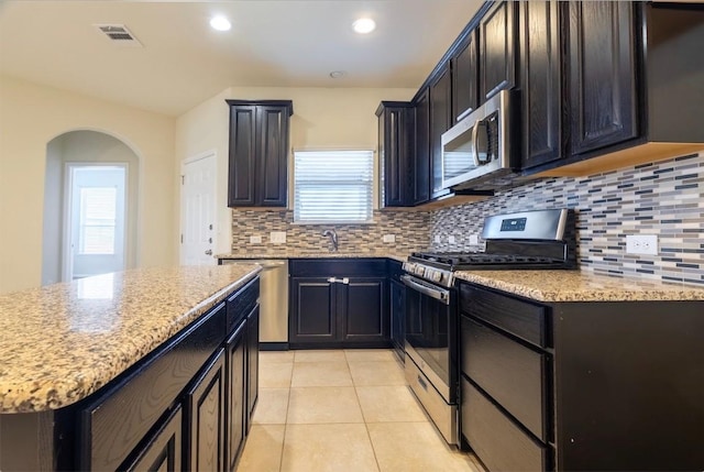 kitchen featuring light tile patterned floors, visible vents, arched walkways, appliances with stainless steel finishes, and light stone countertops