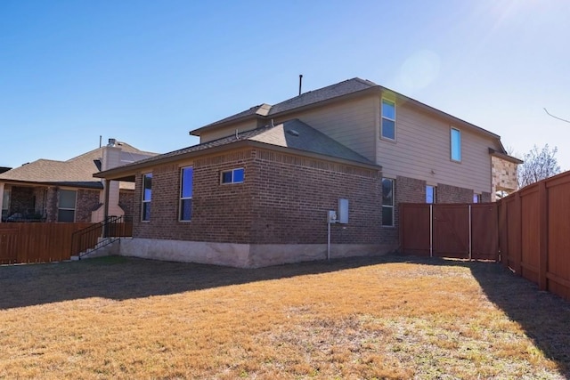 rear view of house featuring a fenced backyard, a lawn, and brick siding