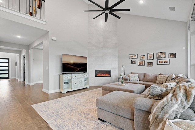 living room with a high ceiling, a fireplace, wood finished floors, visible vents, and baseboards