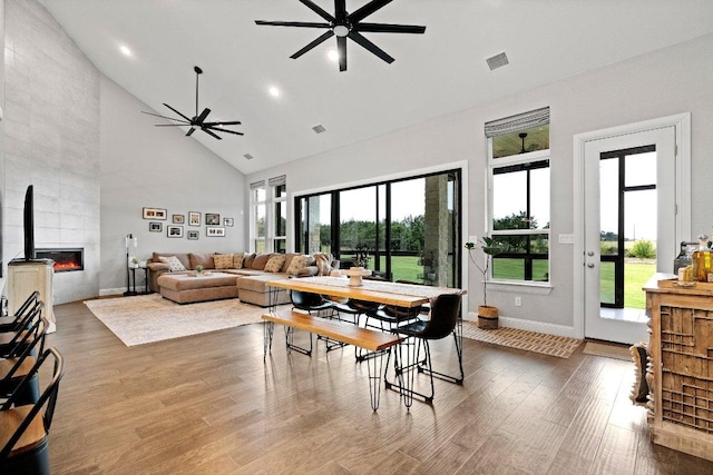 living room featuring high vaulted ceiling, a tile fireplace, wood finished floors, visible vents, and a ceiling fan