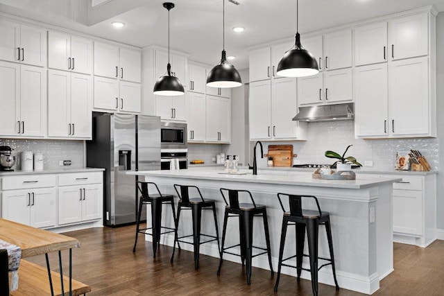 kitchen with stainless steel appliances, a breakfast bar, light countertops, and under cabinet range hood