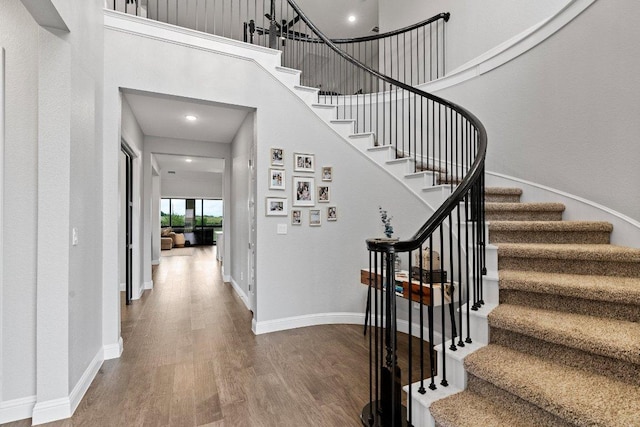 staircase featuring a high ceiling, baseboards, and wood finished floors