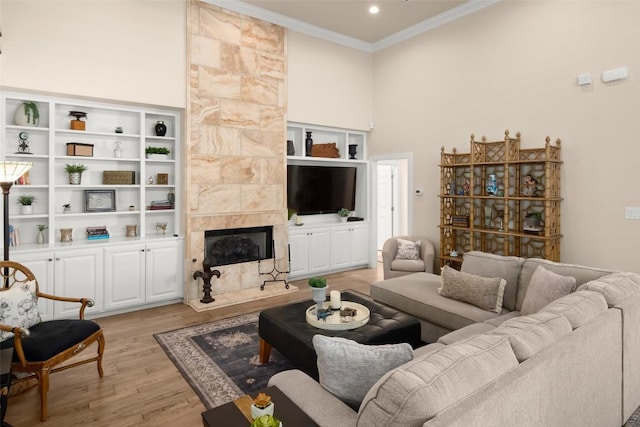 living room featuring ornamental molding, a premium fireplace, a towering ceiling, and light wood-style floors