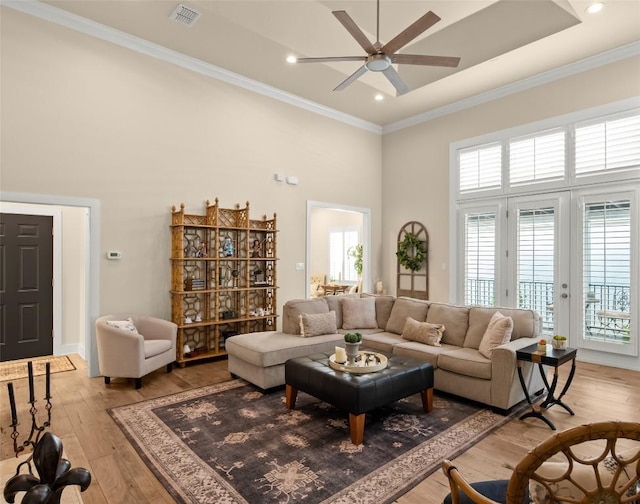 living room featuring ornamental molding, visible vents, light wood-style flooring, and a high ceiling