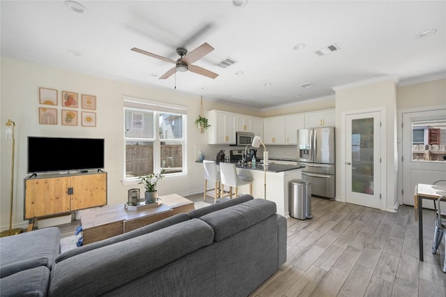 living room with ornamental molding, visible vents, light wood-style flooring, and a ceiling fan