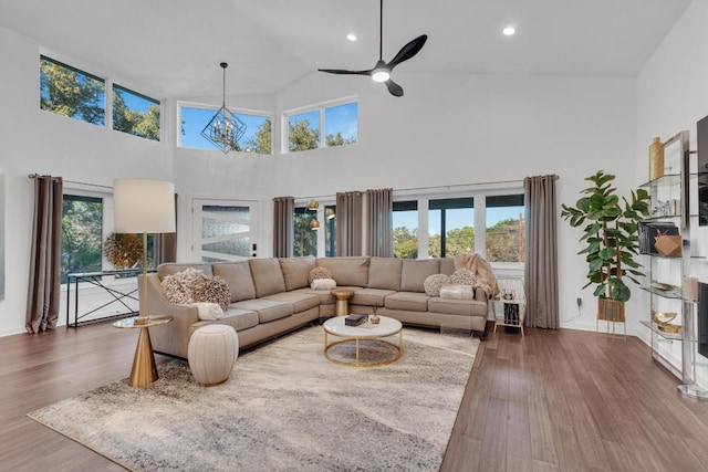 living room with ceiling fan with notable chandelier, recessed lighting, wood finished floors, and a towering ceiling