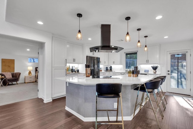 kitchen featuring light countertops, black fridge, island exhaust hood, white cabinets, and dark wood-style flooring