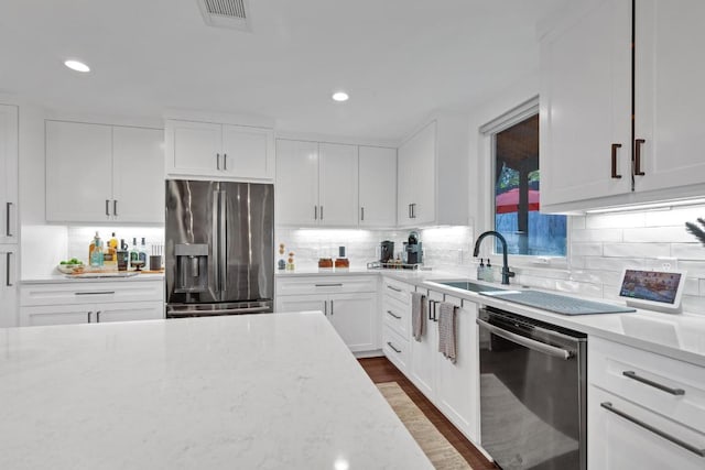 kitchen with dark wood-type flooring, light stone countertops, white cabinets, stainless steel appliances, and a sink