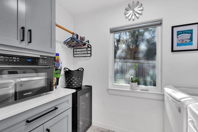 laundry area with baseboards, beverage cooler, cabinet space, marble finish floor, and separate washer and dryer