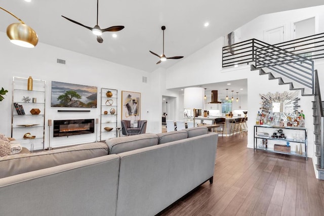 living room featuring visible vents, ceiling fan, dark wood finished floors, a glass covered fireplace, and high vaulted ceiling