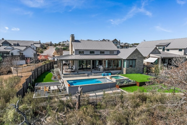 rear view of property with a pool with connected hot tub, a lawn, a standing seam roof, metal roof, and a fenced backyard