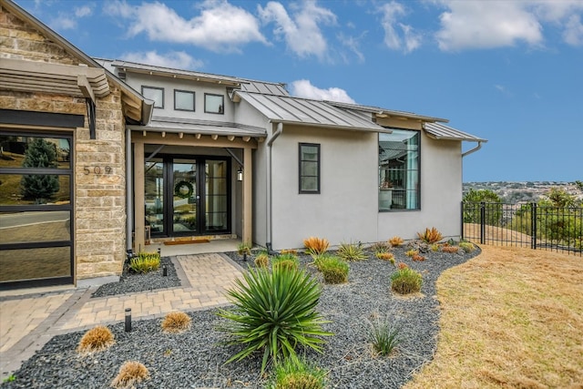 view of exterior entry featuring stone siding, metal roof, a standing seam roof, fence, and stucco siding