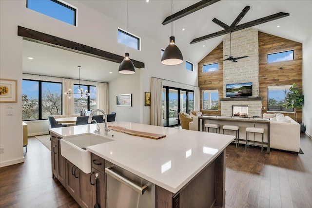 kitchen with a sink, dishwasher, beamed ceiling, dark wood finished floors, and a center island with sink