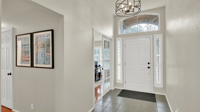 foyer entrance featuring baseboards, an inviting chandelier, tile patterned floors, and a healthy amount of sunlight