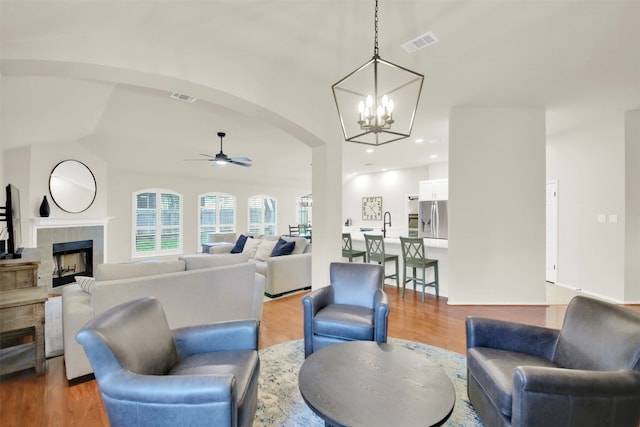 living room featuring light wood-type flooring, ceiling fan, visible vents, and a tiled fireplace