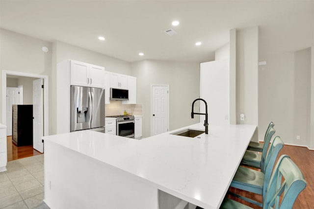 kitchen with light countertops, appliances with stainless steel finishes, a sink, a peninsula, and a kitchen bar