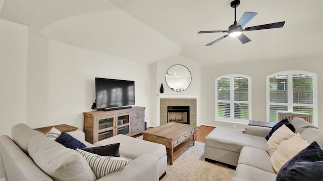 living room featuring lofted ceiling, ceiling fan, a tiled fireplace, and light wood-style flooring