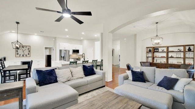 living room featuring arched walkways, light wood finished floors, lofted ceiling, recessed lighting, and ceiling fan with notable chandelier