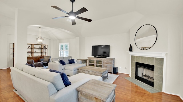 living area featuring ceiling fan with notable chandelier, lofted ceiling, a fireplace, and wood finished floors