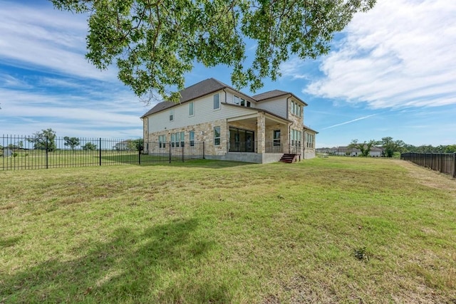 back of house featuring stone siding, a lawn, and a fenced backyard