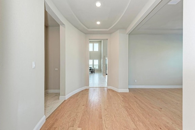 interior space featuring light wood-style floors, baseboards, a tray ceiling, and recessed lighting