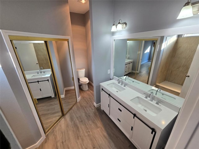 bathroom with baseboards, tiled shower, toilet, wood finished floors, and vanity