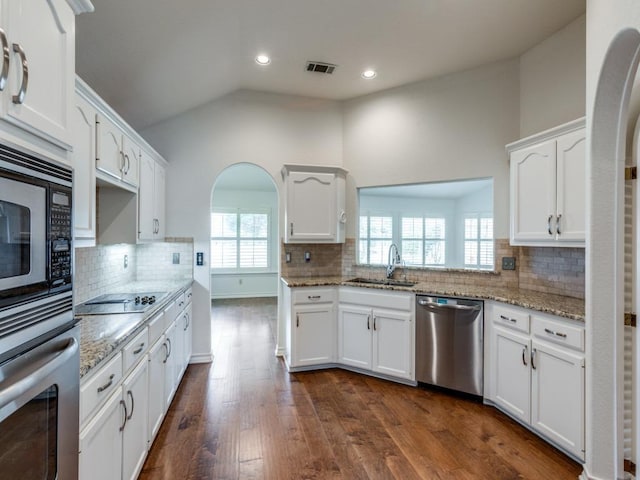 kitchen with white cabinets, appliances with stainless steel finishes, light stone countertops, vaulted ceiling, and a sink