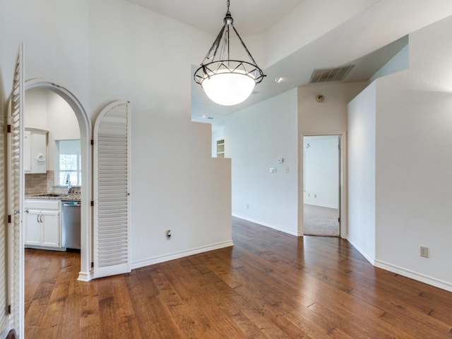 interior space with arched walkways, a sink, wood finished floors, visible vents, and baseboards