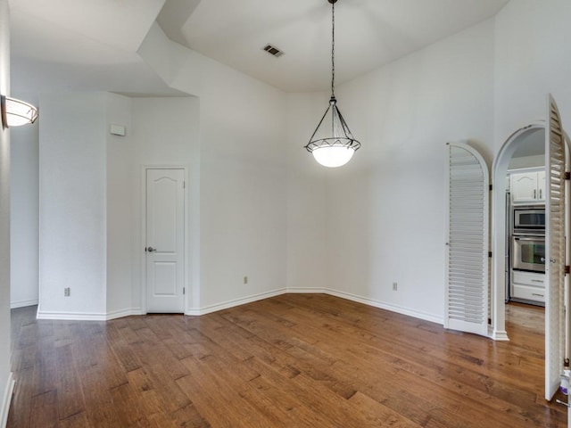 unfurnished dining area featuring arched walkways, wood finished floors, a towering ceiling, visible vents, and baseboards