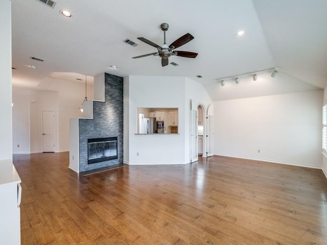 unfurnished living room with a fireplace, visible vents, ceiling fan, vaulted ceiling, and wood finished floors