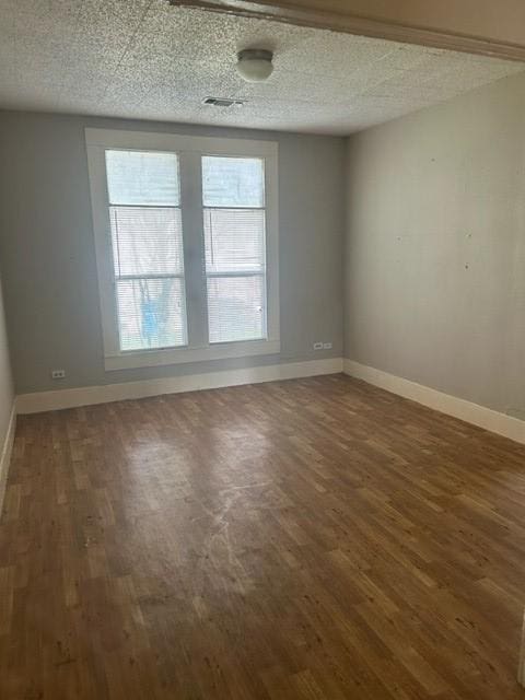 empty room featuring dark wood-style floors, a textured ceiling, visible vents, and baseboards