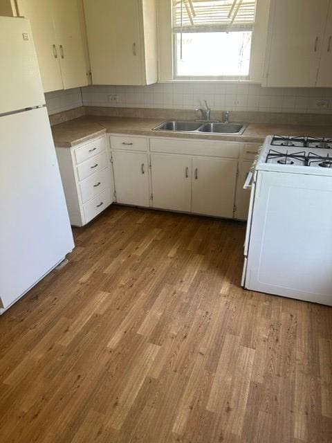 kitchen featuring white appliances, light wood finished floors, white cabinets, decorative backsplash, and a sink