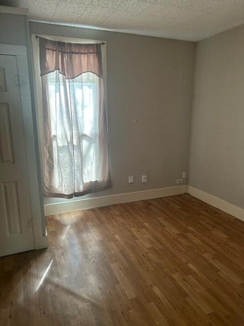 spare room featuring a textured ceiling, baseboards, and wood finished floors