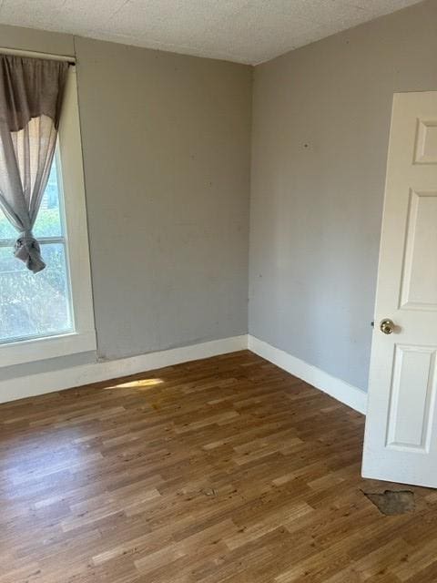 unfurnished room with a textured ceiling, baseboards, and wood finished floors