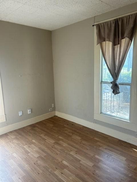 empty room featuring a textured ceiling, wood finished floors, and baseboards