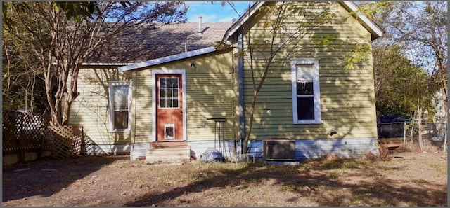 rear view of house featuring entry steps, cooling unit, and fence