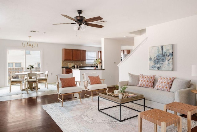 living room featuring ceiling fan with notable chandelier, hardwood / wood-style flooring, visible vents, and baseboards