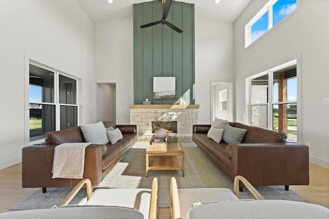 living room with baseboards, a ceiling fan, wood finished floors, a high ceiling, and a fireplace